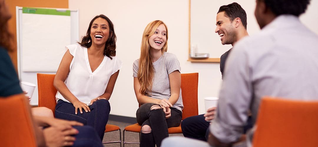 Group of diverse people smiling and talking in a casual meeting setting.