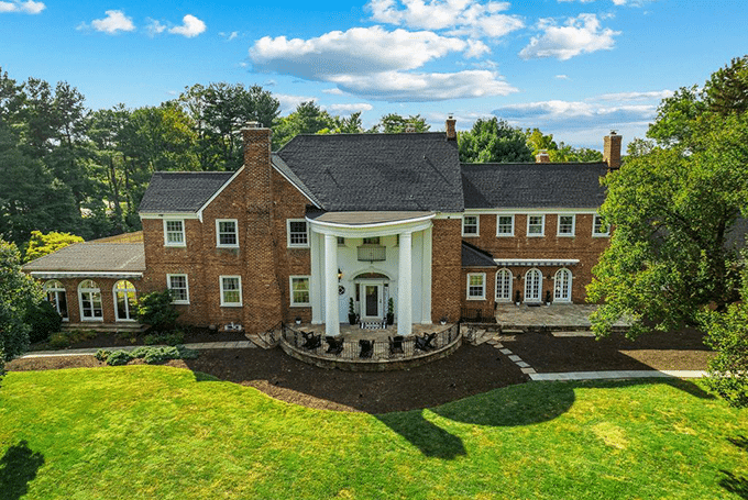 Grand brick mansion with white columns surrounded by lush greenery and clear blue sky.