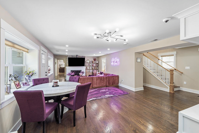Modern living and dining area with purple chairs, wooden floors, and neon wall art. Cozy, stylish interior design.