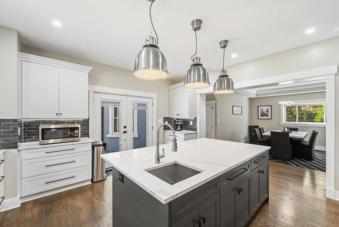Modern kitchen with island, pendant lights, white cabinets, and dining area view in open floor plan.